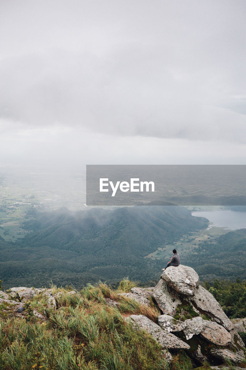 Hiker sitting on rocks against cloudy sky during foggy weather