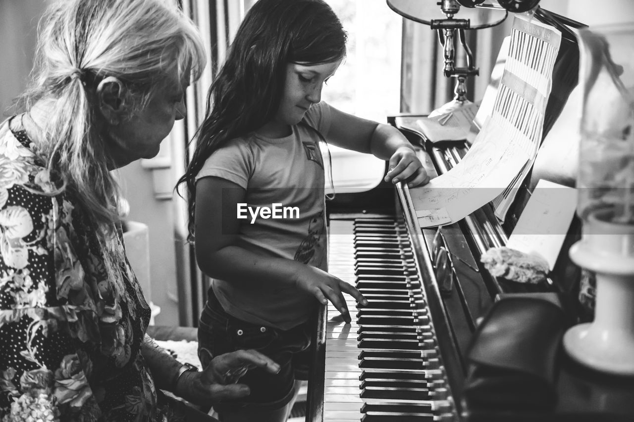 Grandmother teaching piano to granddaughter at home