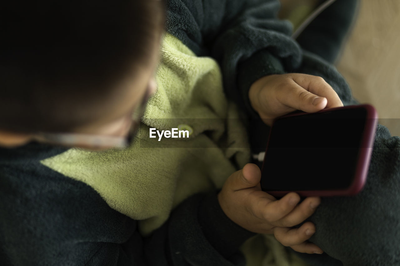 Closeup portrait of a boy who looks into phone sitting on floor, playing on the phone on charging