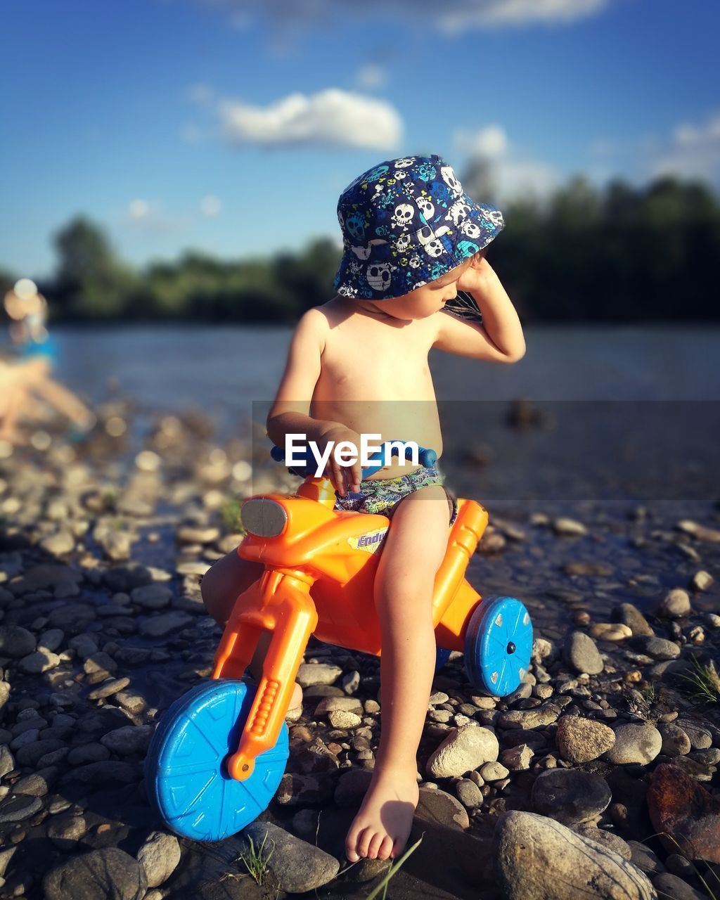 Full length of shirtless boy with tricycle on beach against sky