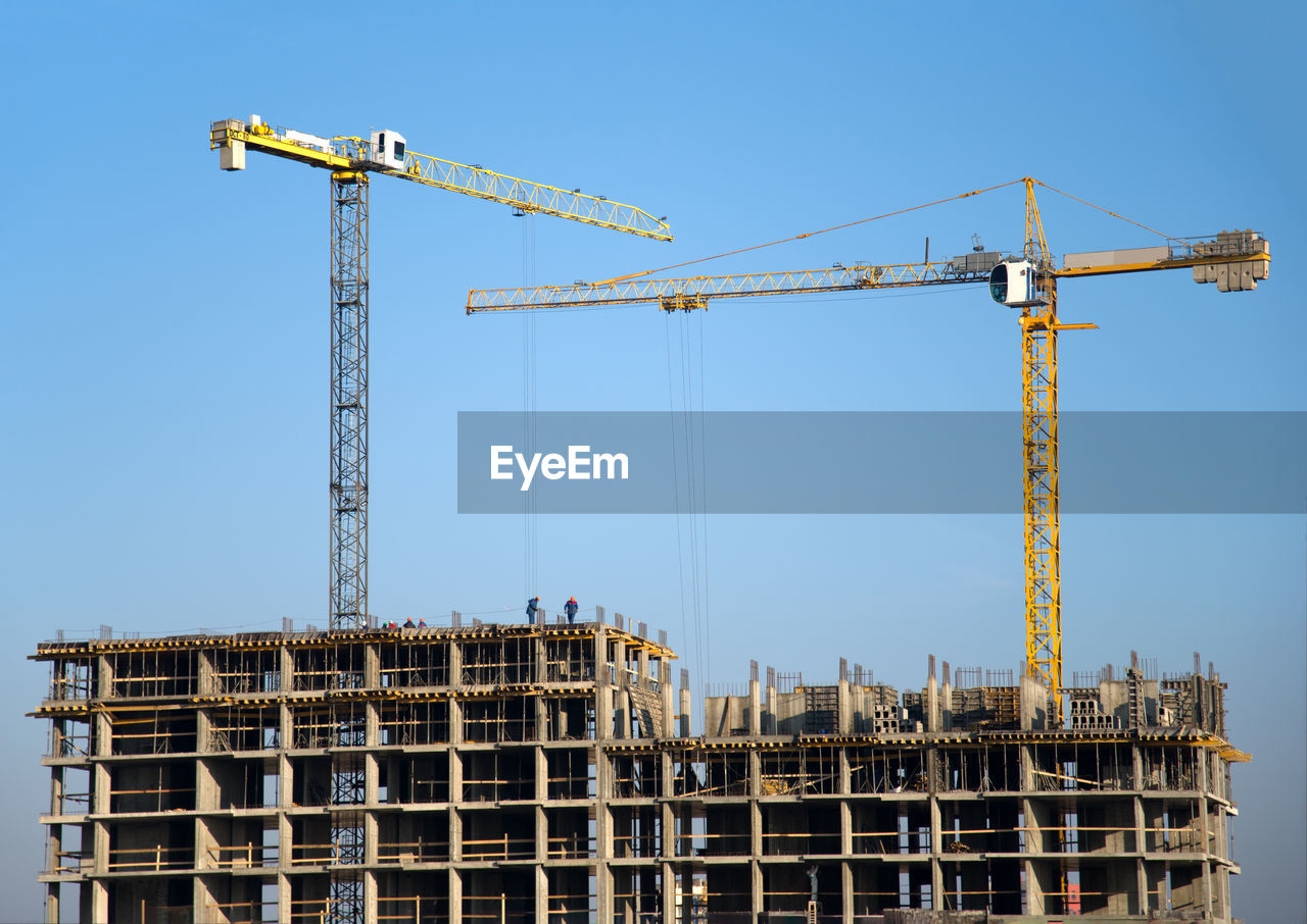 CRANES AT CONSTRUCTION SITE AGAINST SKY