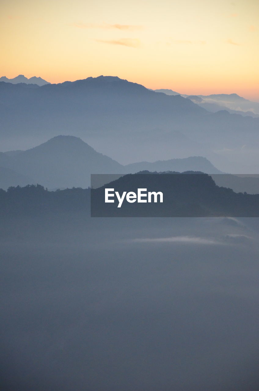 Scenic view of mountains in foggy weather during sunrise