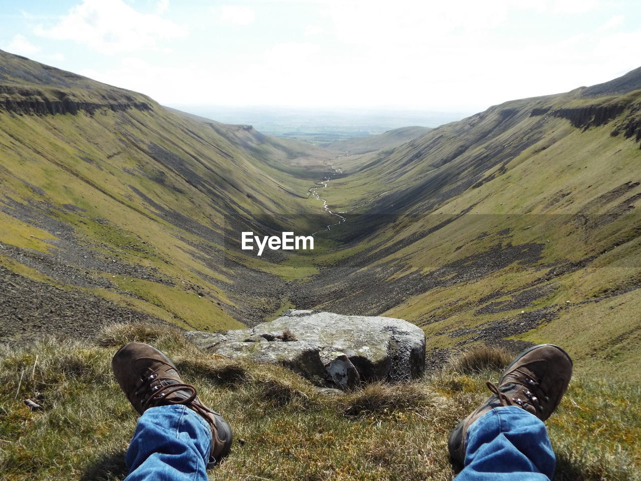 Low section of man sitting on hill against sky