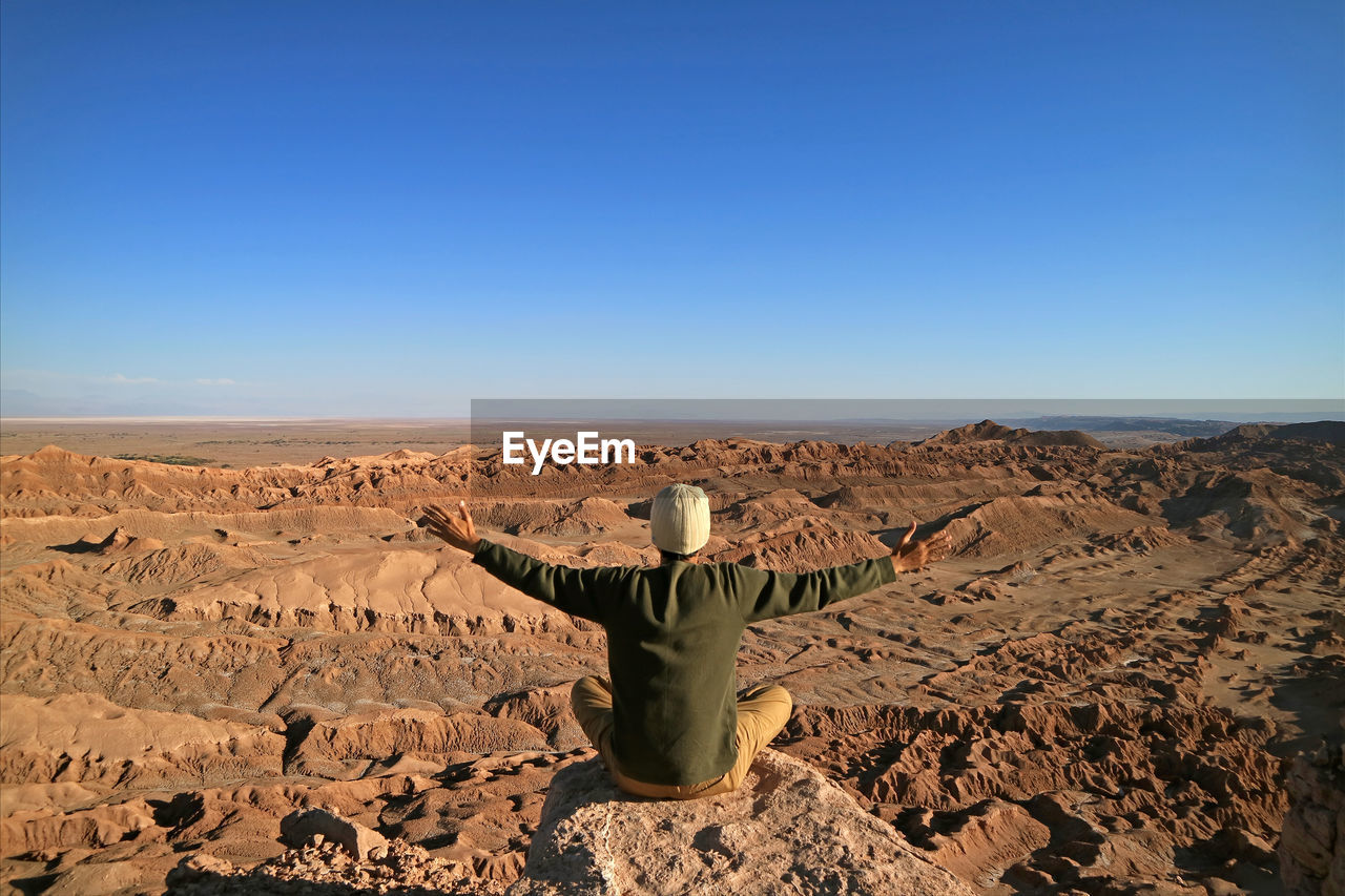 Rear view of man walking in desert against clear sky