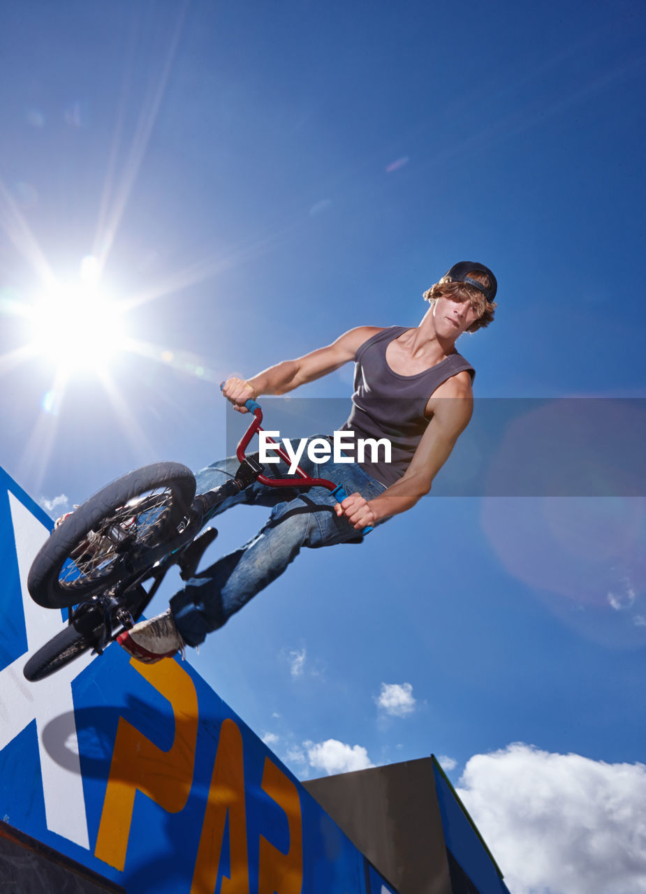 sports, sky, bicycle, adult, blue, one person, low angle view, young adult, sunlight, extreme sports, full length, leisure activity, cycle sport, skill, men, jumping, nature, lifestyles, stunt, bicycle motocross, motion, mid-air, lens flare, activity, recreation, day, sports equipment, vitality, stunt performer, exercising, casual clothing, vehicle, bmx cycling, athlete, motocross, bmx bike, sunny, land vehicle, outdoors, skateboard park, joy, person, sports clothing, balance, practicing, determination, sun, teenager, fun, exhilaration, cloud, emotion, adventure