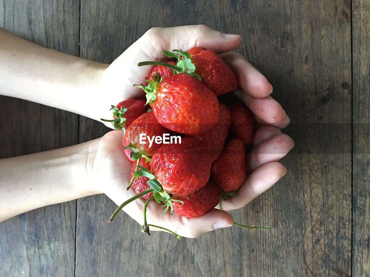 Close-up of hands holding strawberries over wooden table