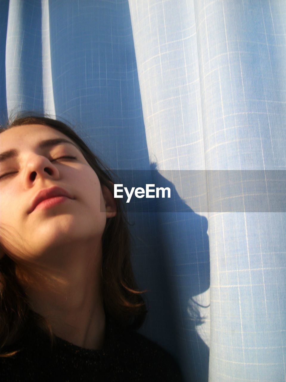 Close-up of young woman with eyes closed by curtain at home