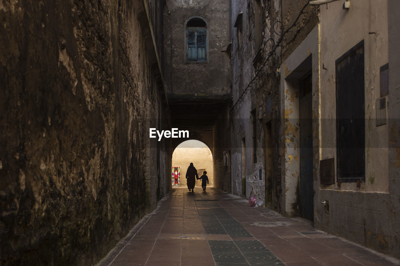 Rear view of people walking in alley amidst buildings in city