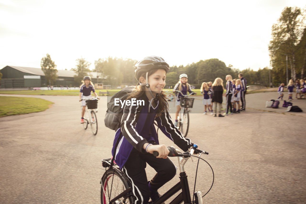 Girl cycling on footpath with friends against sky