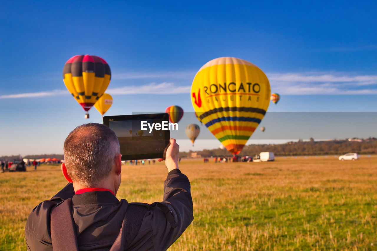 REAR VIEW OF MAN WITH BALLOONS IN FIELD