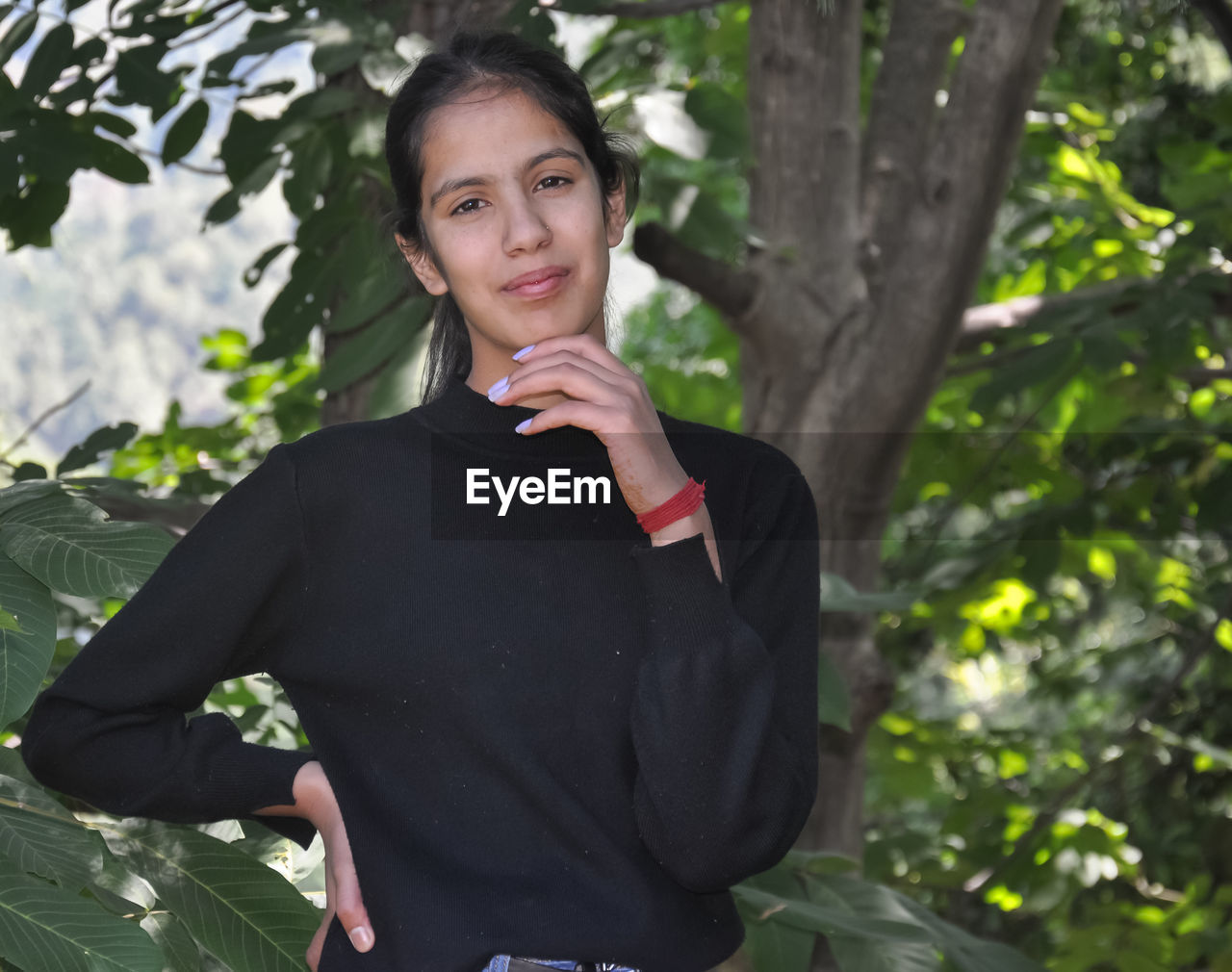 A beautiful indian young girl posing in nature with her hand on chin and hips with looking at camera