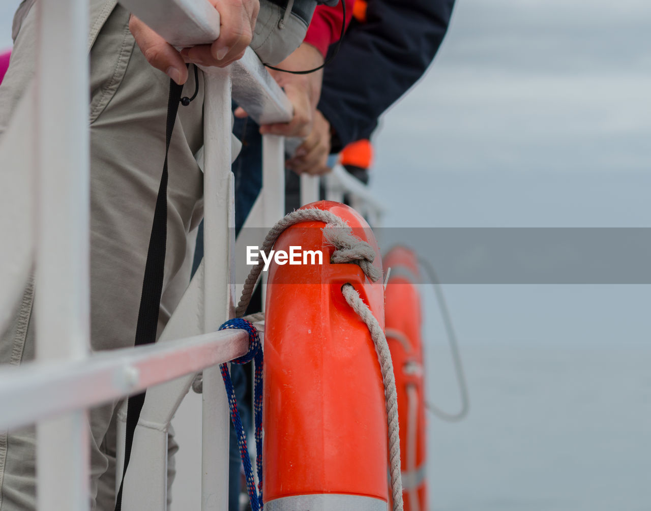 Midsection of men standing by railing with life belts on boat at sea