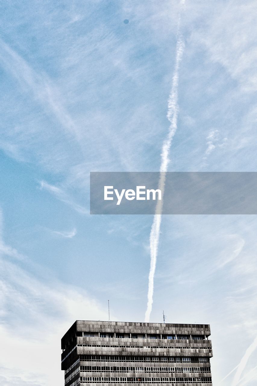 Low angle view of building against vapor trail in sky