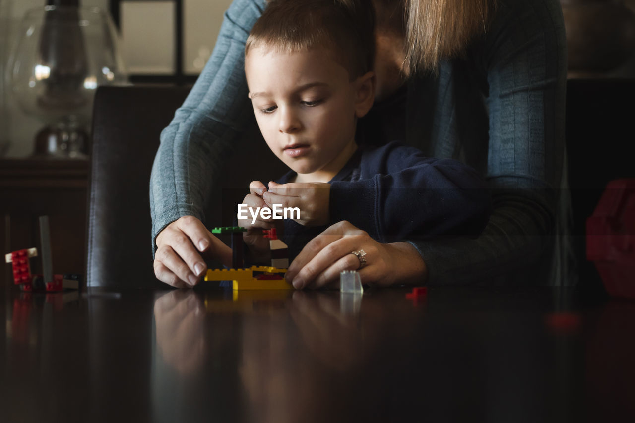 Midsection of mother assisting son in making toy blocks at table