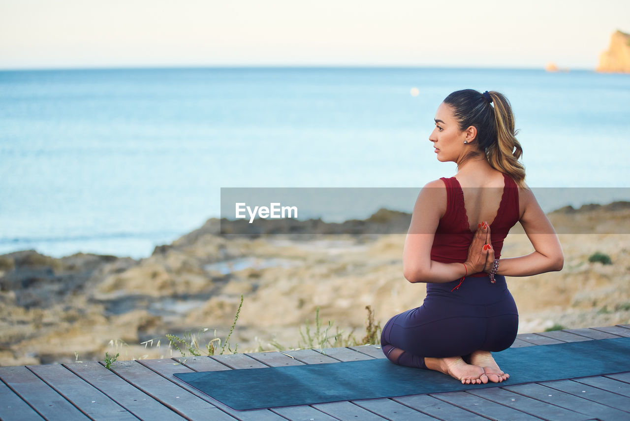 WOMAN SITTING ON BEACH AGAINST SEA