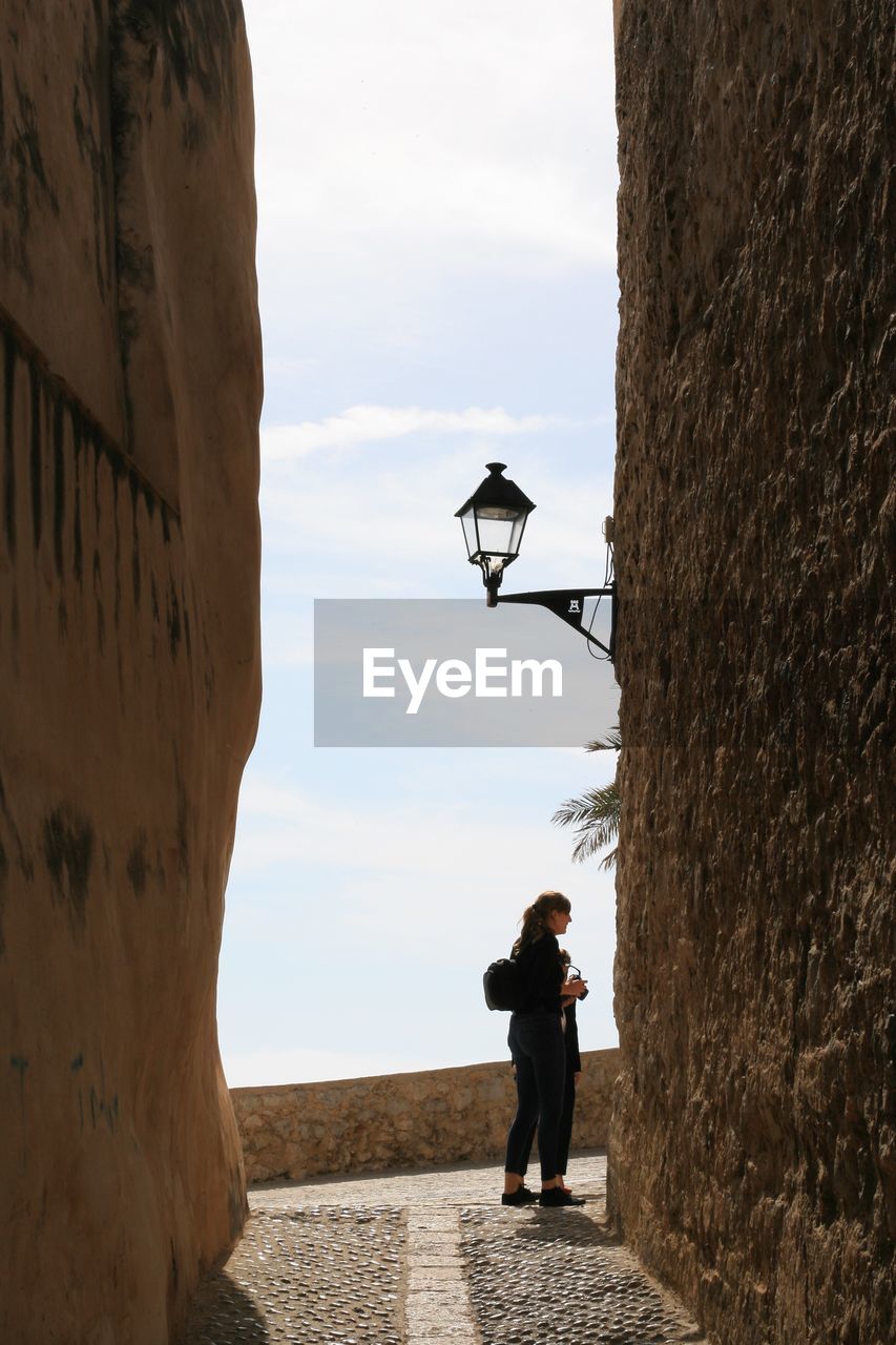 Full length of woman standing on walkway amidst wall