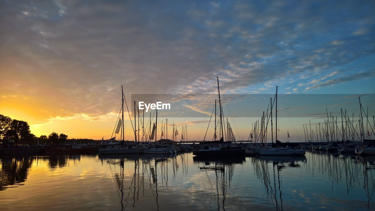 SAILBOATS MOORED IN HARBOR AGAINST SKY DURING SUNSET