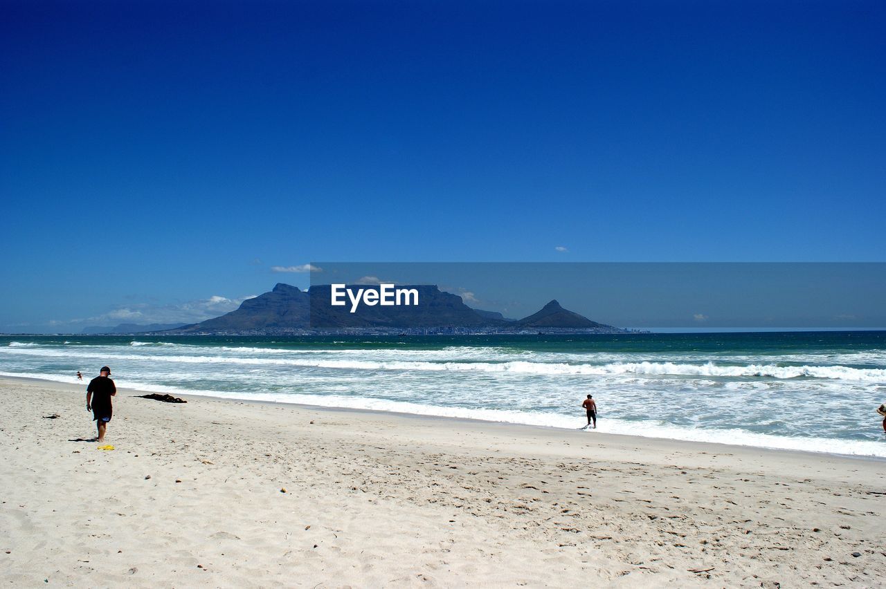 People on beach against clear blue sky