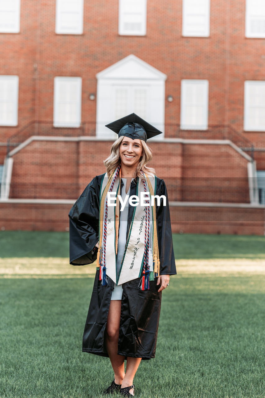 PORTRAIT OF A SMILING YOUNG WOMAN STANDING AGAINST WALL