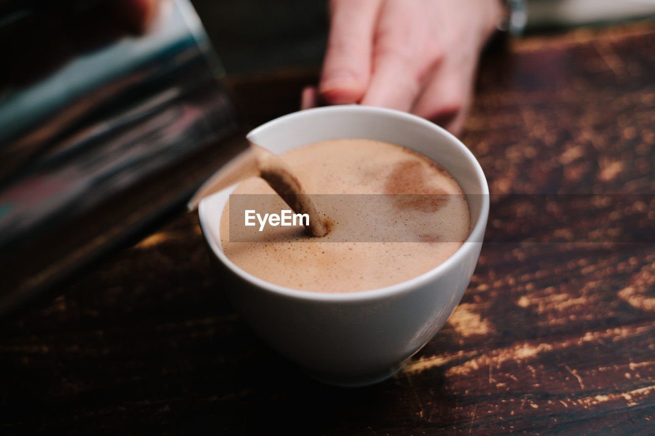 Cropped hand pouring coffee in cup on table