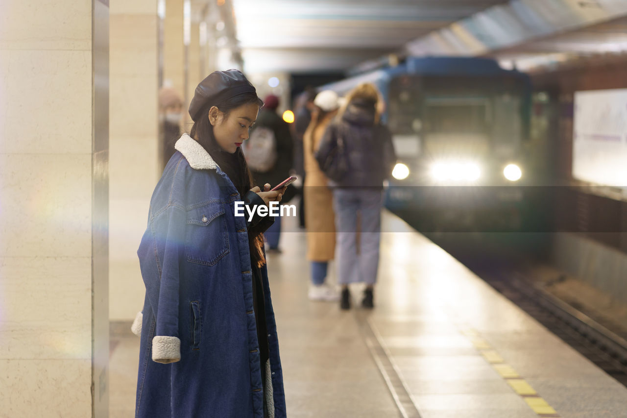 Japanese girl busy in cellphone at metro station with train arriving. young woman message to friend