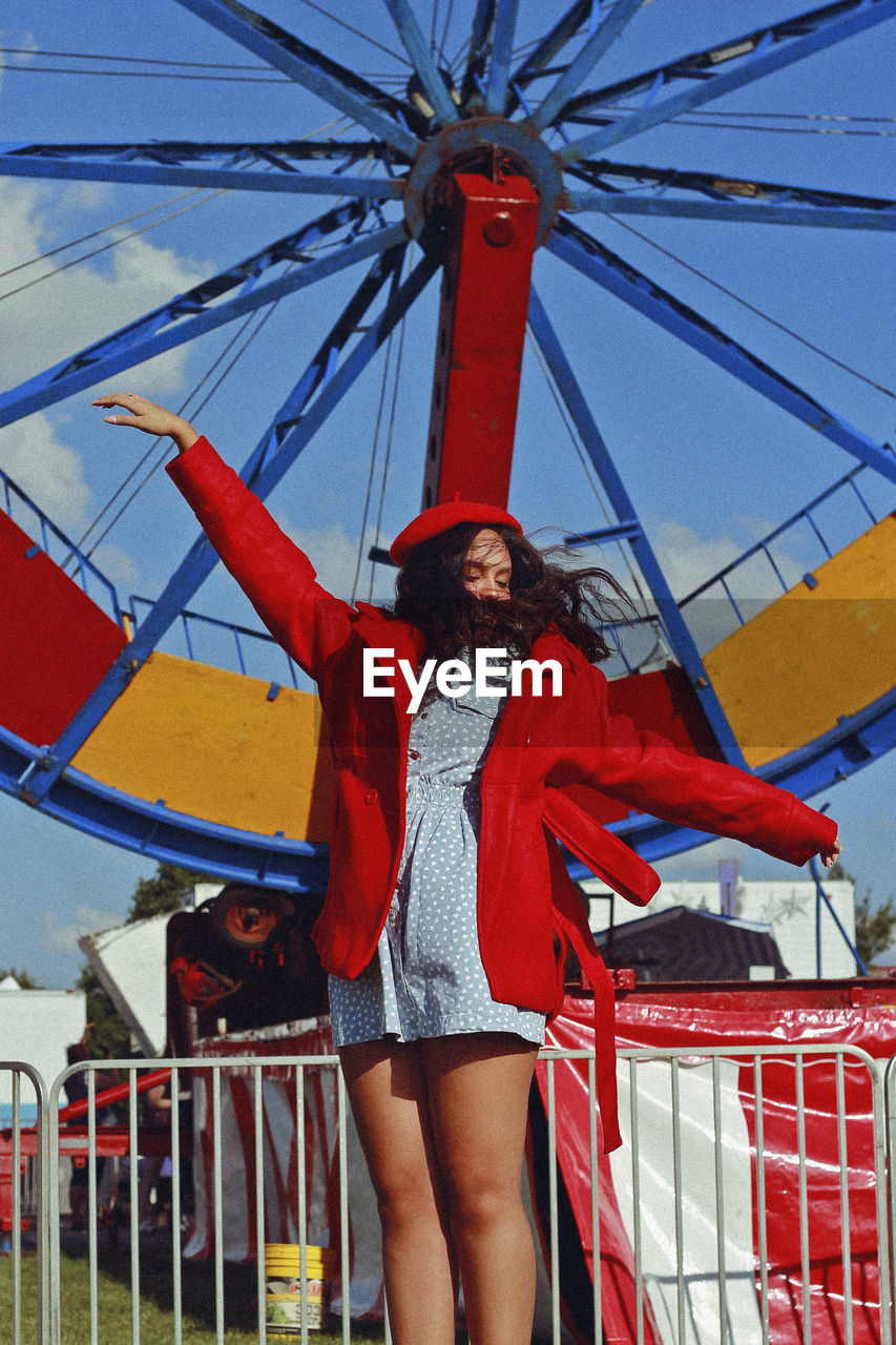 Teenager girl with arms outstretched jumping against ferris wheel 