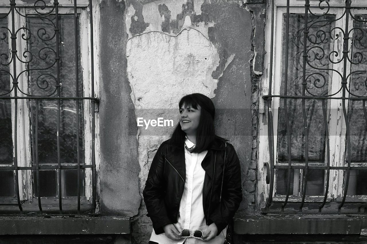 Young woman looking away while standing by old building