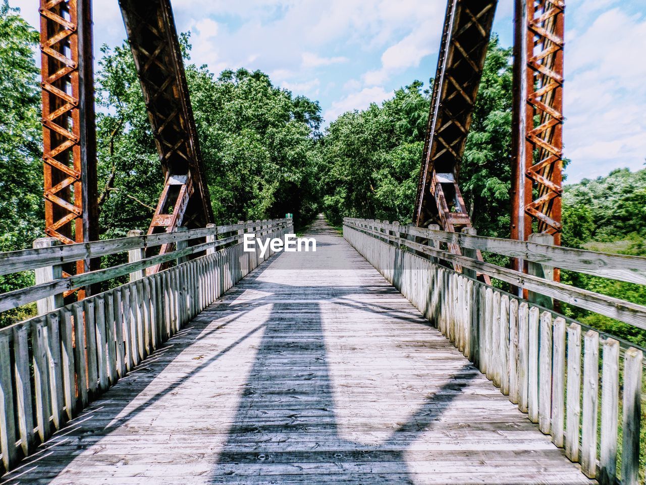 Bridge leading towards trees during sunny day