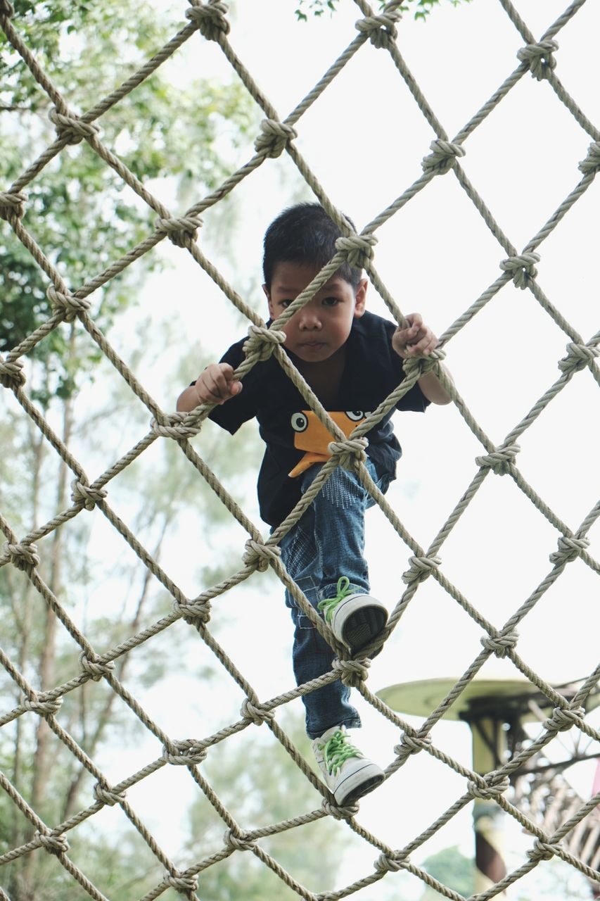 Portrait of cute boy climbing on play equipment at park