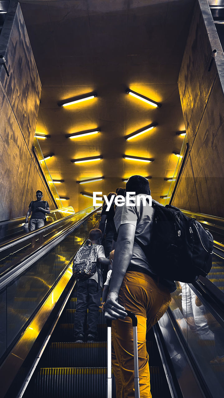 escalator, architecture, transportation, adult, indoors, staircase, subway station, men, one person, person, mode of transportation, clothing, public transport, motion, railing, travel, light, built structure, steps and staircases, public transportation, transport, subway, yellow, city, rail transportation, technology