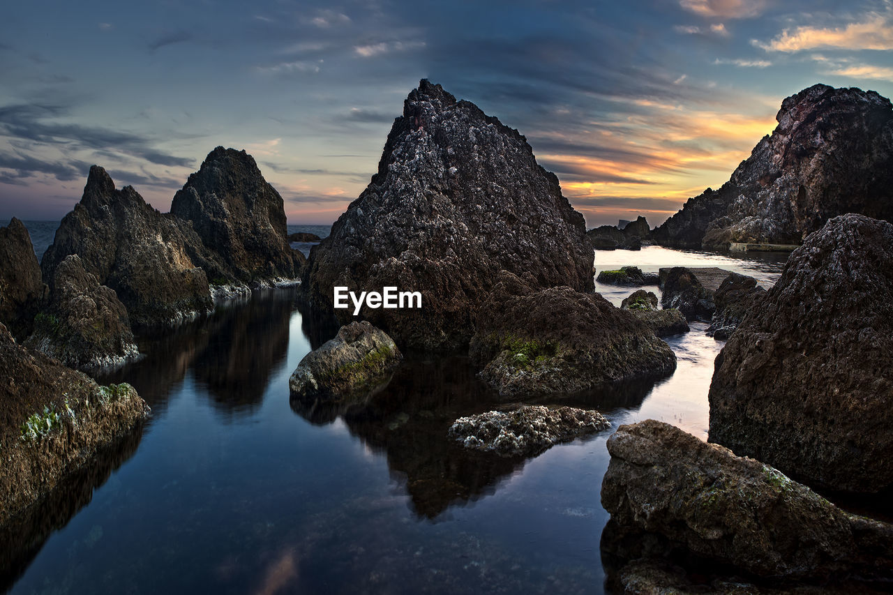 Rocks on shore against sky during sunset