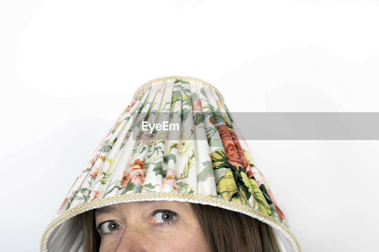 Mature woman with lamp shade on head against white background