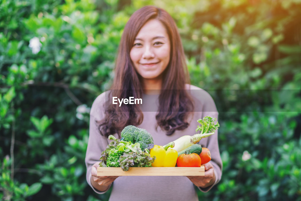 Portrait of smiling woman holding food against plants