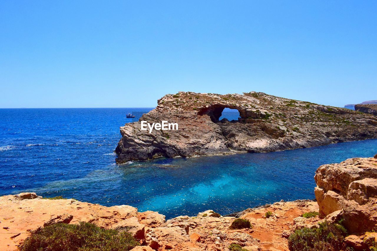 Rock formations by sea against clear blue sky