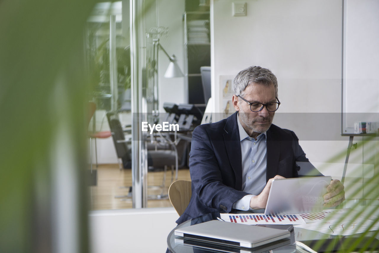 Successful businessman sitting in board room using digital tablet