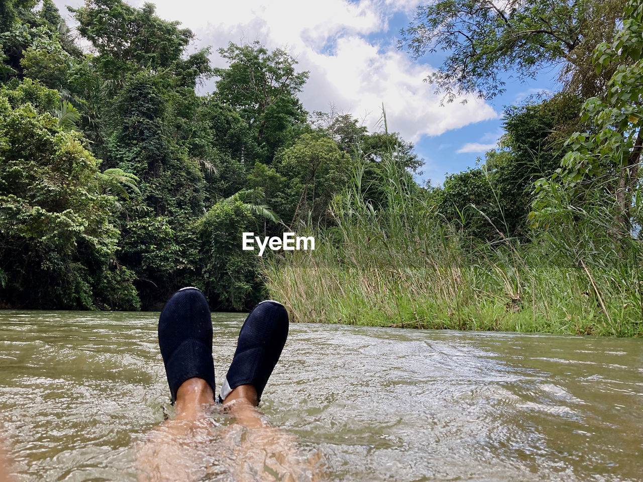 plant, tree, nature, river, water, leisure activity, human leg, low section, lifestyles, beauty in nature, day, sky, cloud, adult, one person, land, green, relaxation, vacation, outdoors, holiday, trip, limb, men, barefoot, tranquility, women, human foot, growth, beach, scenics - nature, personal perspective, forest, non-urban scene, tranquil scene, shoe, casual clothing, footwear, sitting, human limb