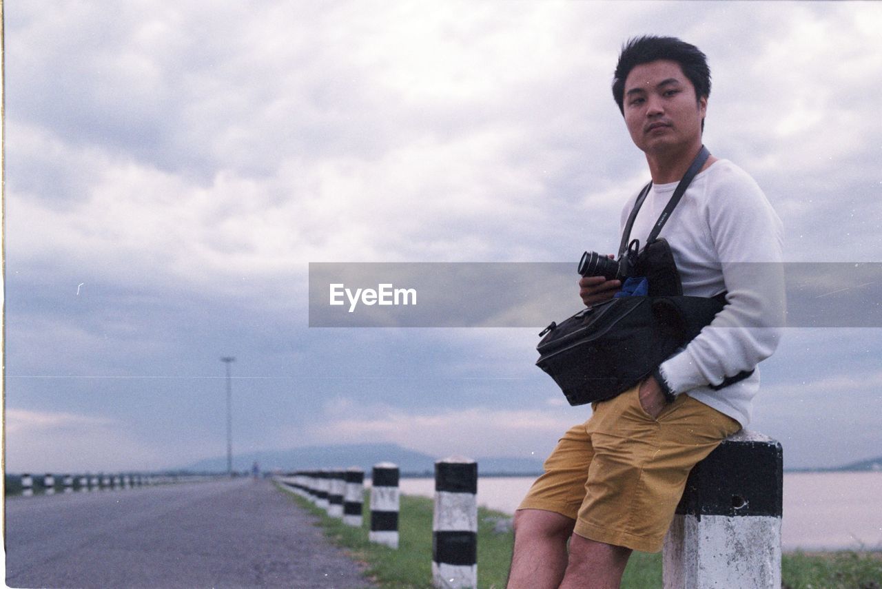 Portrait of man sitting on bollard against sky