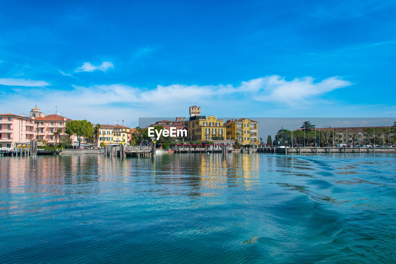 View of city at waterfront against cloudy sky