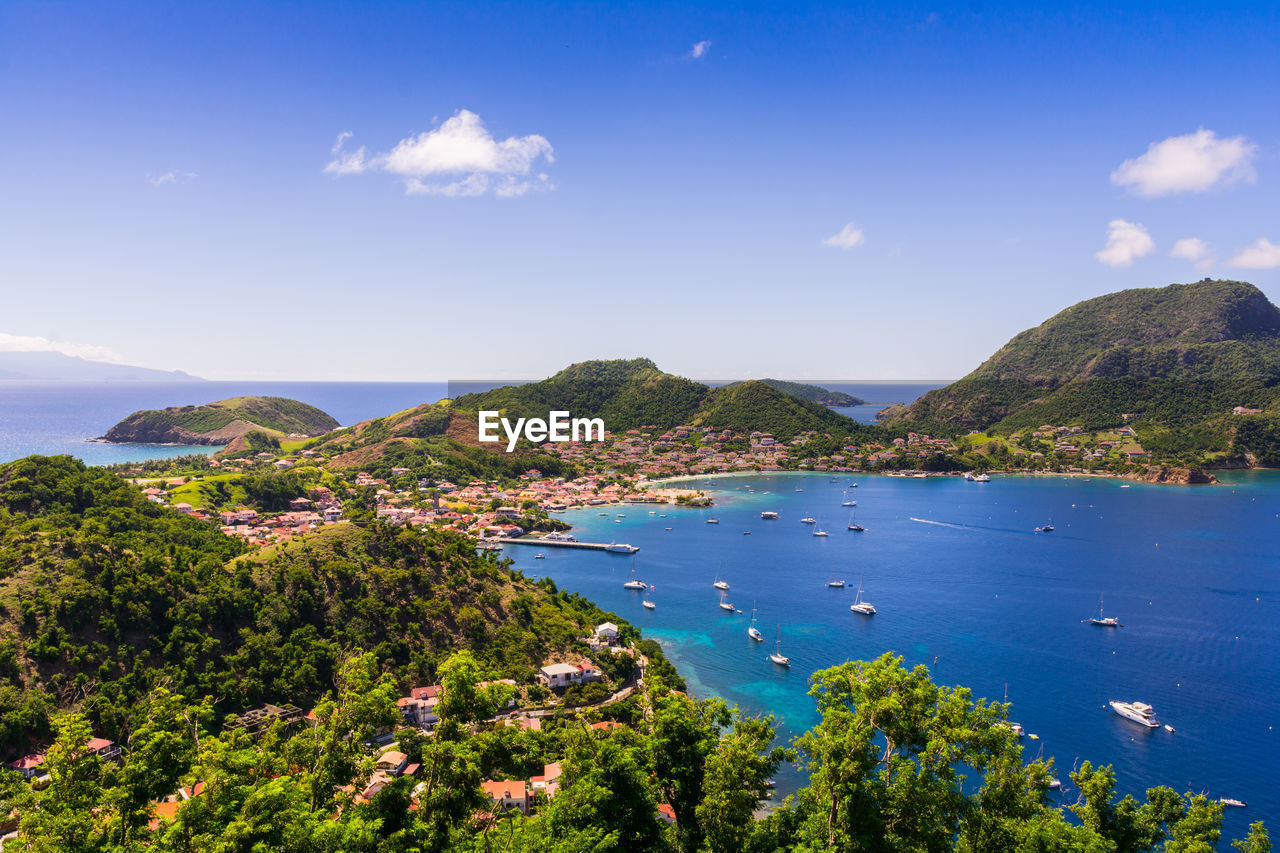 HIGH ANGLE VIEW OF PLANTS AND BAY AGAINST BLUE SKY