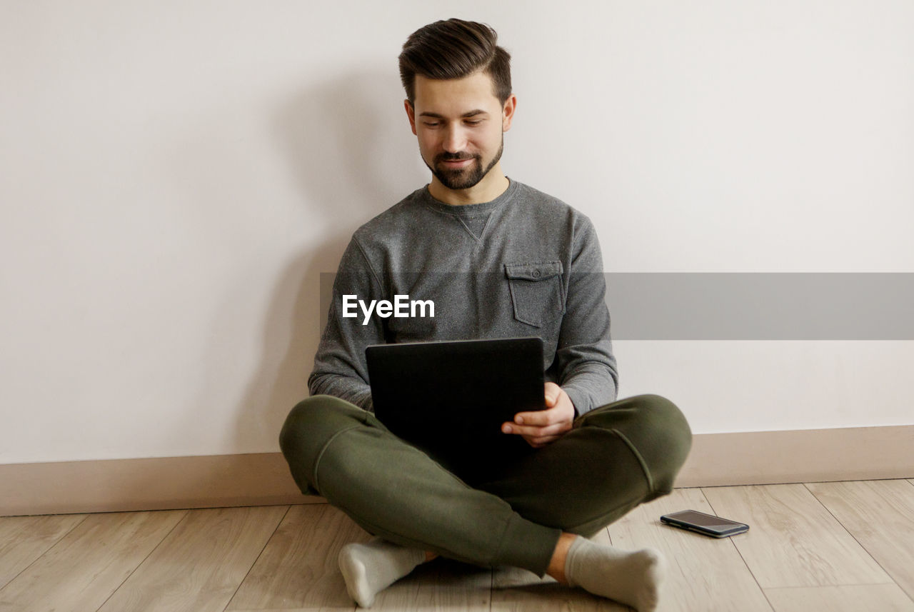 Young man using laptop while sitting on hardwood floor at home