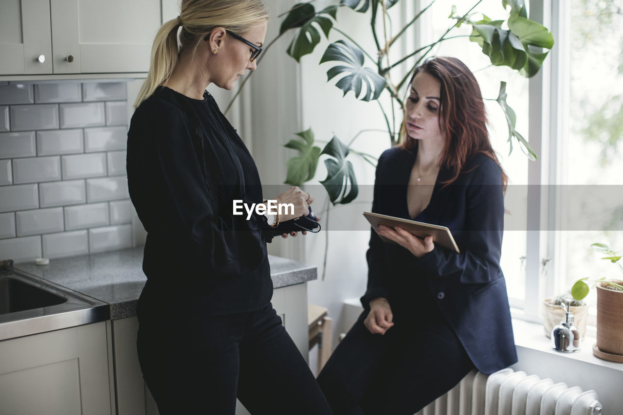 Female colleagues discussing by kitchen counter at home