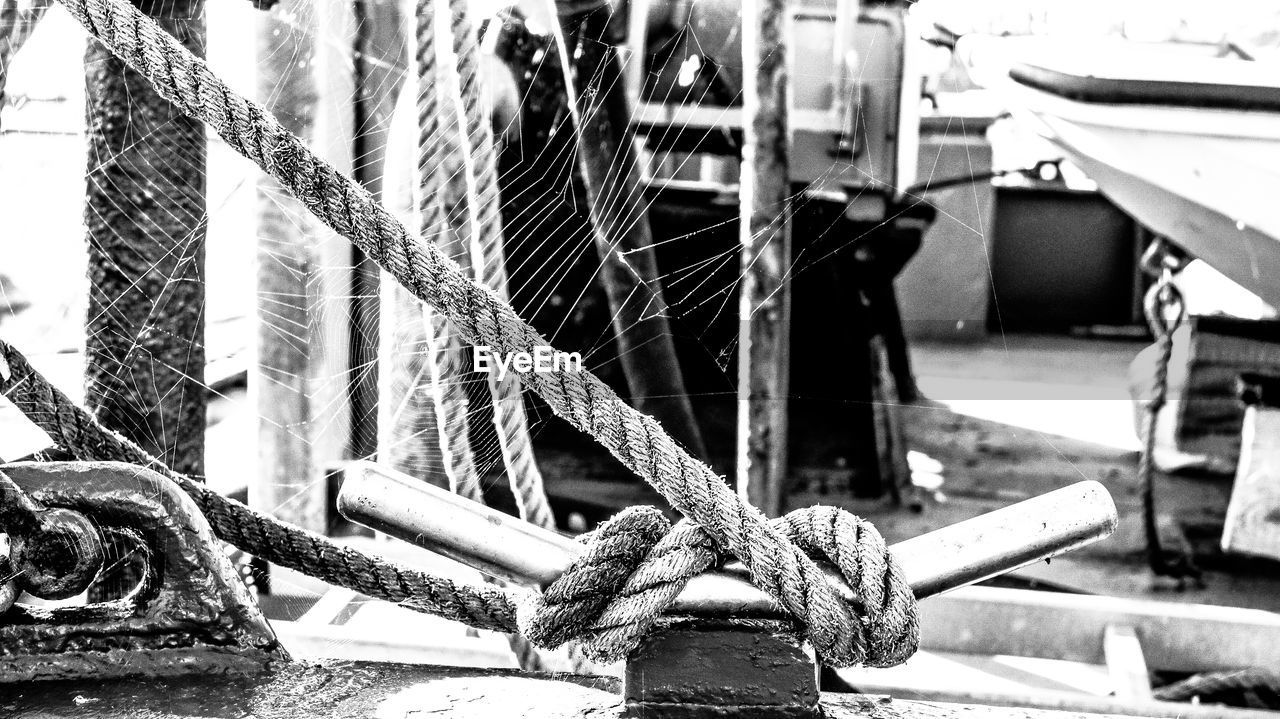 CLOSE-UP OF ROPE TIED TO MOORED HARBOR