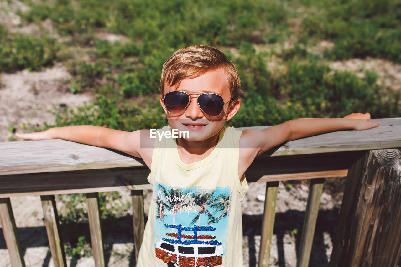 PORTRAIT OF BOY WEARING SUNGLASSES WHILE STANDING ON WOOD