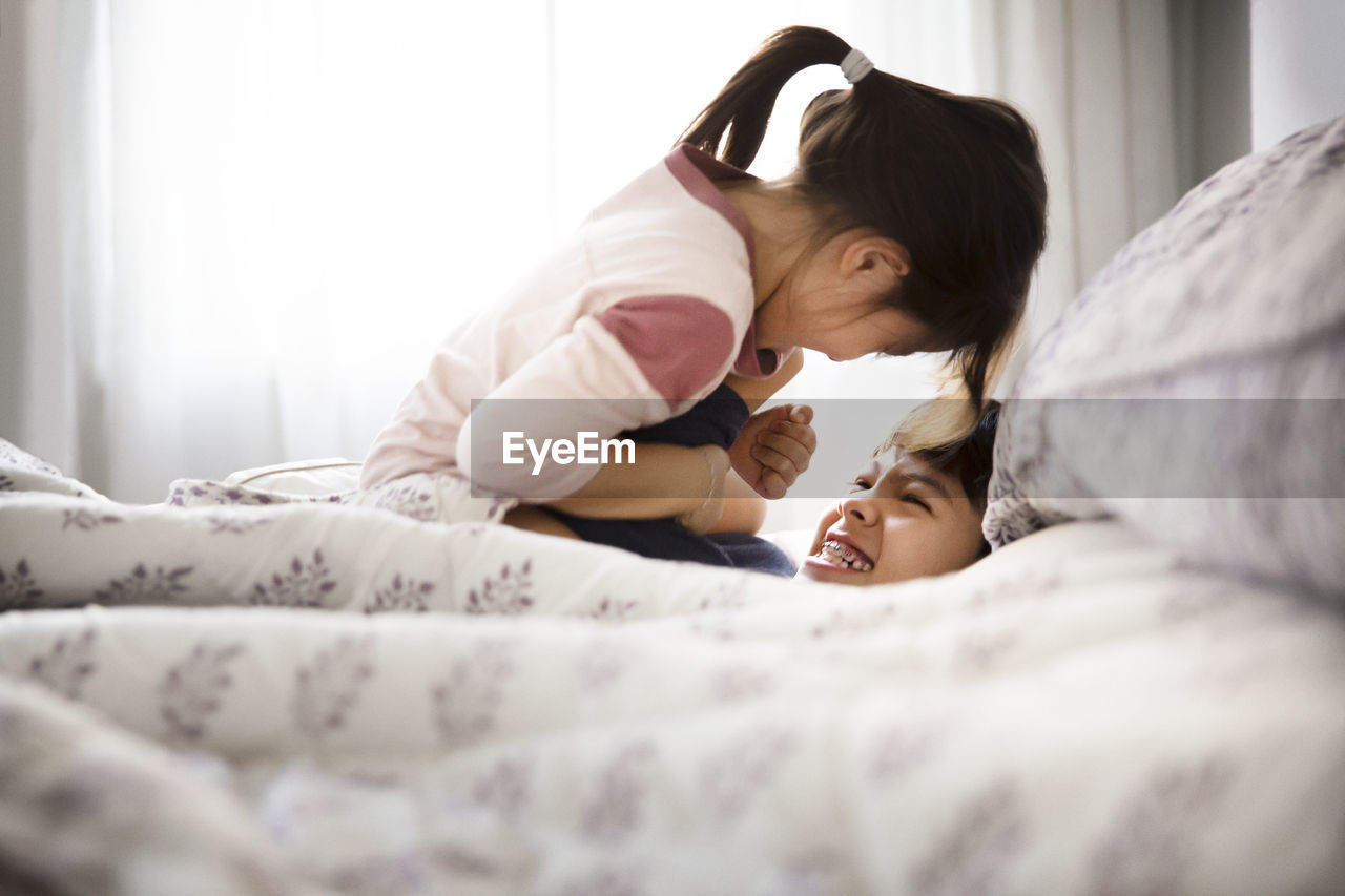 Siblings playing on bed at home