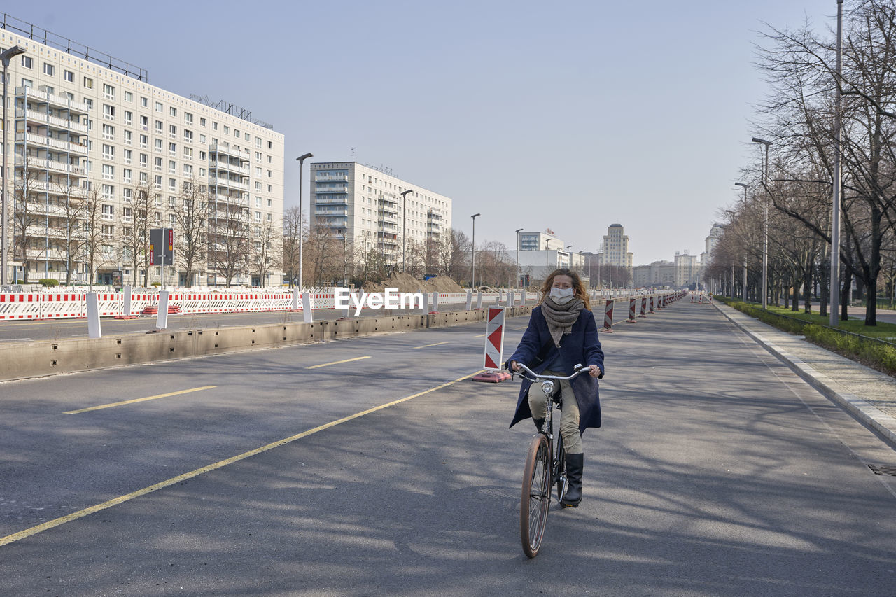 Woman wearing mask riding bicycle on road in city