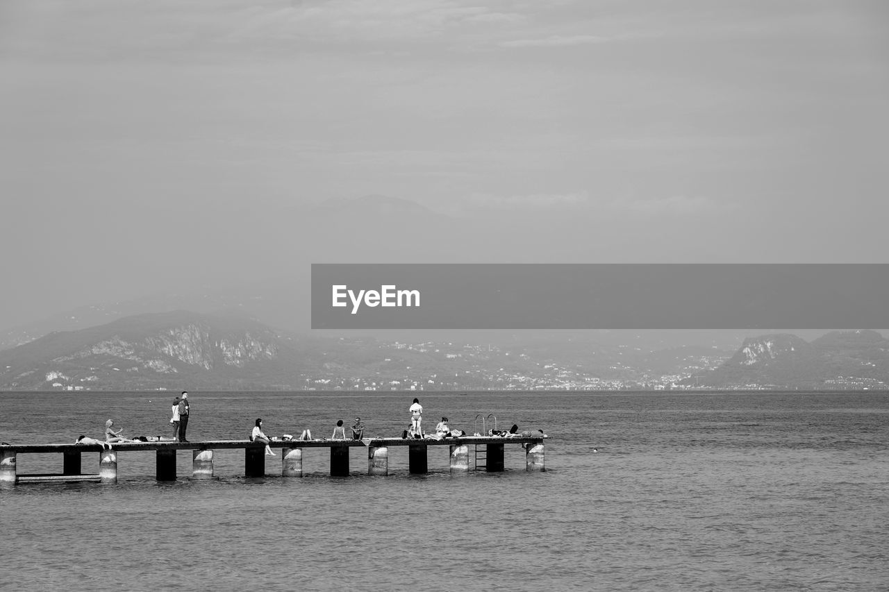 GROUP OF PEOPLE ON PIER OVER SEA AGAINST SKY