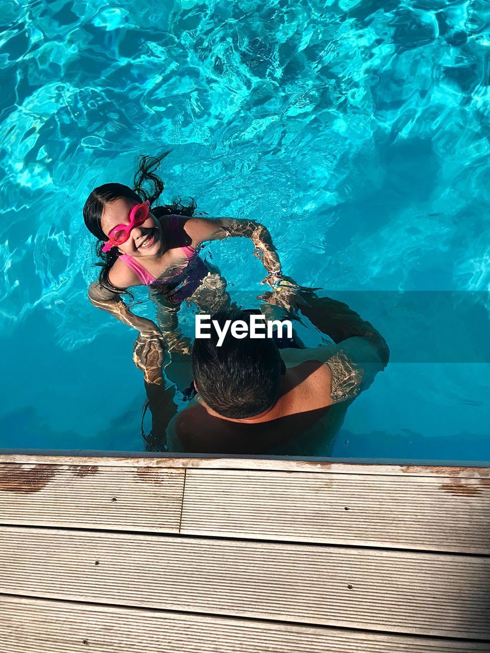 High angle view of father assisting daughter in swimming pool