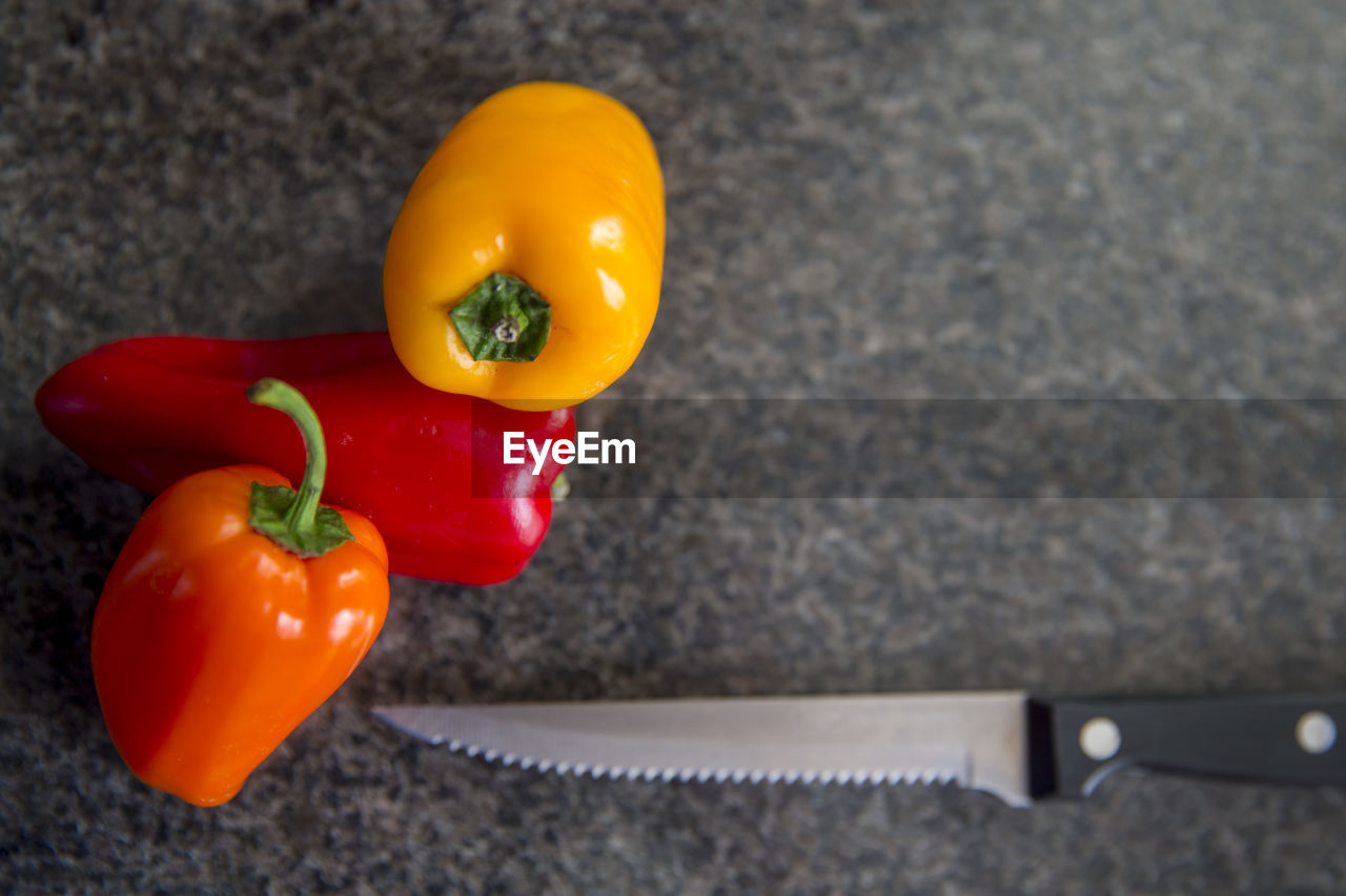 High angle view of orange yellow red bell peppers with knife in kitchen