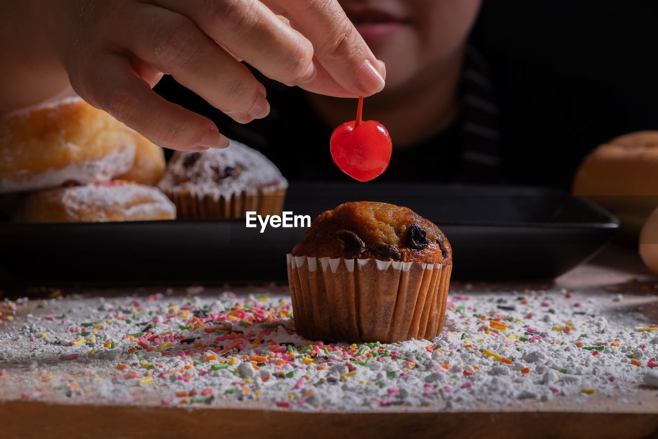 Woman holding cherry over cupcake