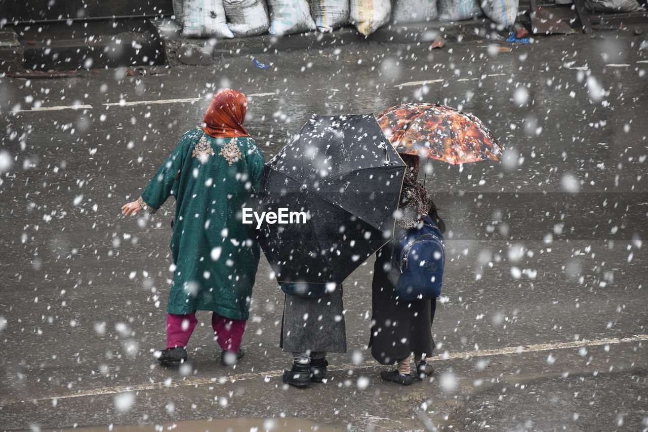 People with umbrella standing on road during snowfall